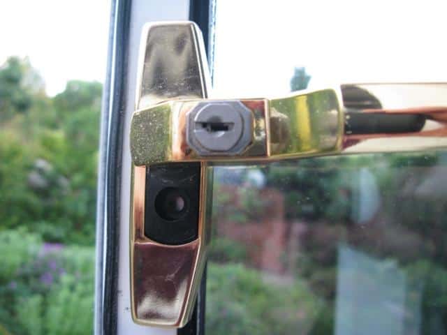 Close-up of a brass uPVC window handle showing the keyhole cylinder and a small black plastic button on the backplate beneath it