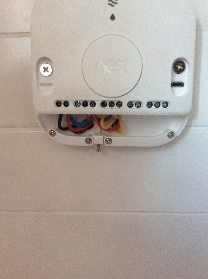 Rear of a Nest thermostat mounted on a wall, showing coloured wires connected to the terminal block on the base plate