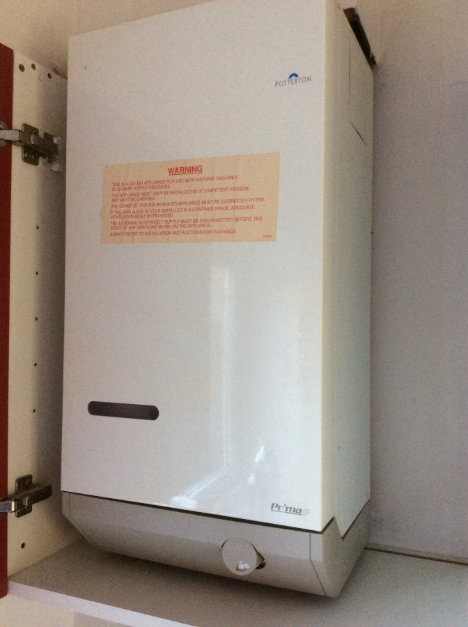 Potterton Prima gas boiler mounted inside a kitchen cupboard with a yellow warning label on the front panel