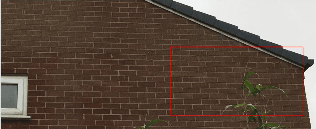 External brick gable wall of a UK semi-detached house with a red rectangle highlighting the junction between the brickwork and the sloping roof line near the eaves.