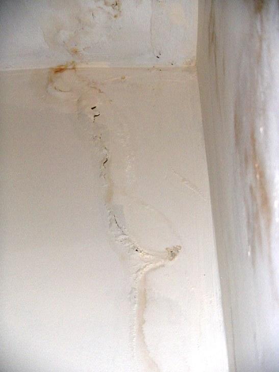Close-up of cracked and bubbling plaster beside a chimney breast, with brown water stain marks running down the wall from the ceiling junction