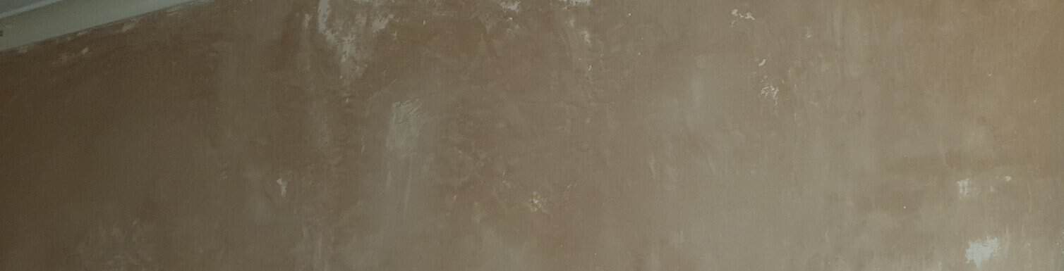 Close-up of a freshly plastered wall surface showing patchy drying, with darker brown damp areas contrasting against lighter dried sections.