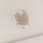 Close-up of a white MDF surface showing a patch where shellac primer has lifted and flaked away, exposing the bare MDF beneath.