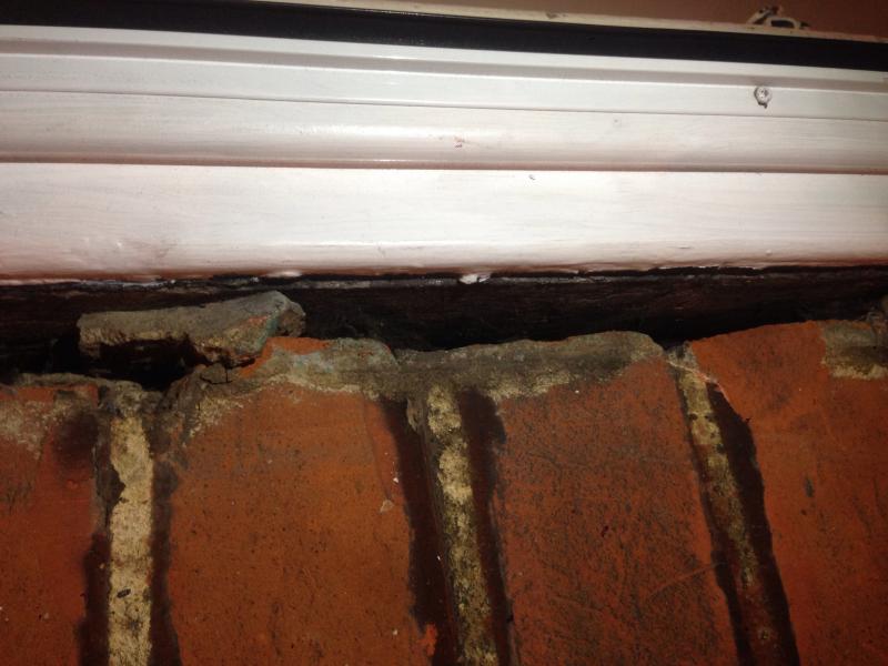 Close-up of a gap between a white uPVC door frame and the surrounding brickwork, showing crumbled mortar and exposed brick beneath the frame sill