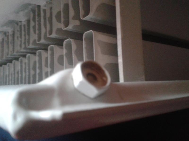 Close-up of a radiator bleed valve with the square-drive spindle sheared off, leaving only the hexagonal brass body visible at the end of the radiator header.