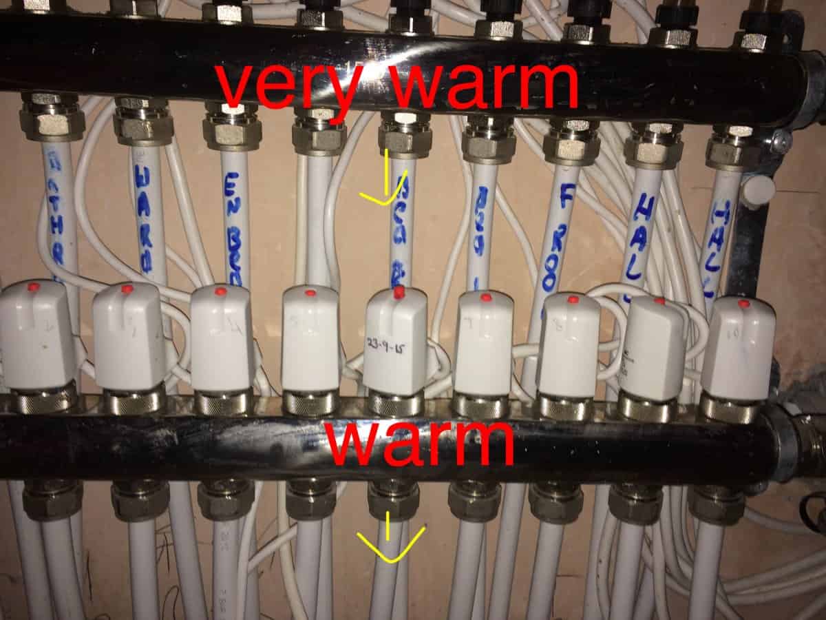 UFH manifold with annotations showing the flow bar labelled very warm and the return bar labelled warm, with yellow arrows pointing to a single pipe on each bar.