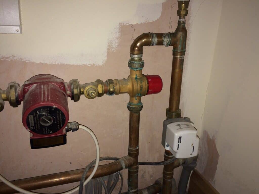 Underfloor heating pump, blending valve with red temperature dial, and motorised actuator mounted on copper pipework in a plant room.