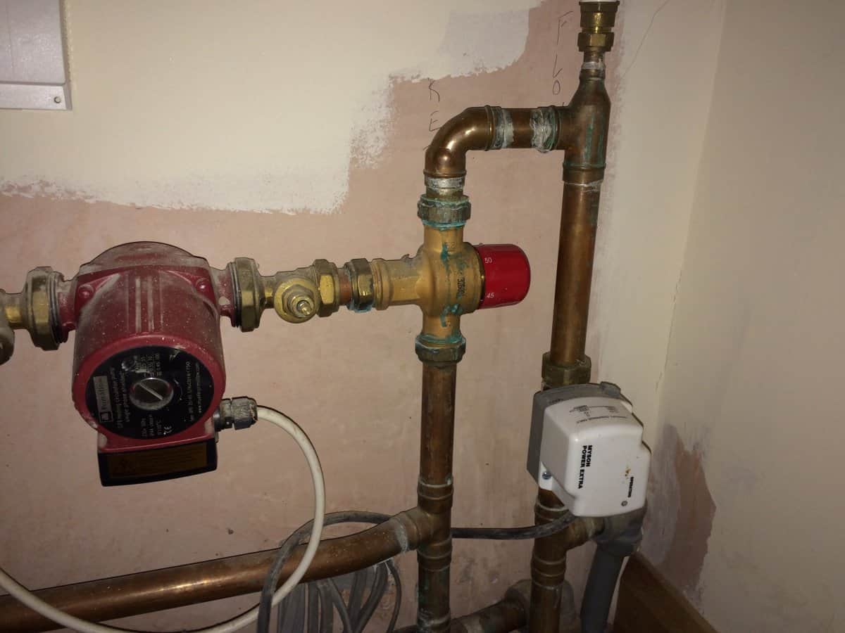 Underfloor heating pump, blending valve with red temperature dial, and motorised actuator mounted on copper pipework in a plant room.