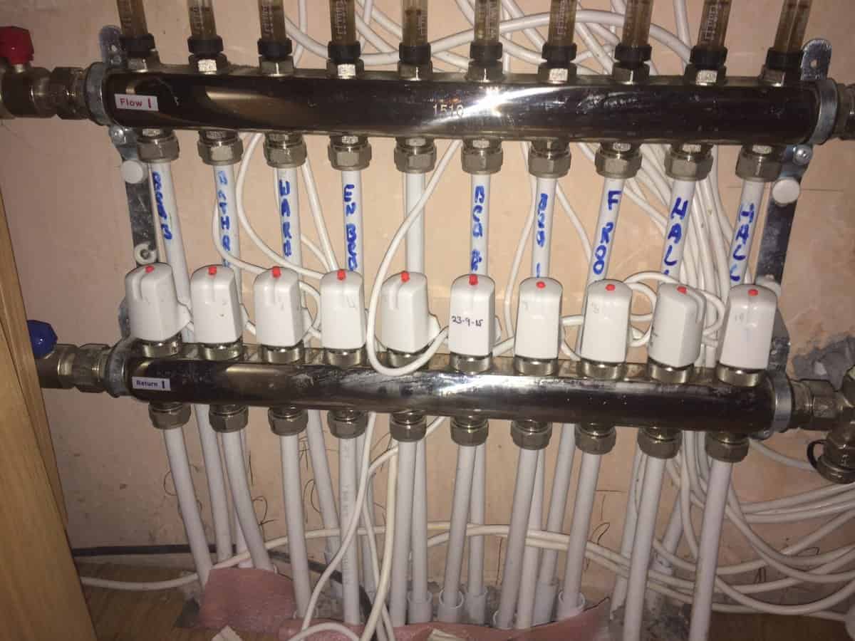 UFH manifold showing flow and return bars with multiple labelled white pipes, flow meters on the flow bar, and white thermal actuators on each return port.