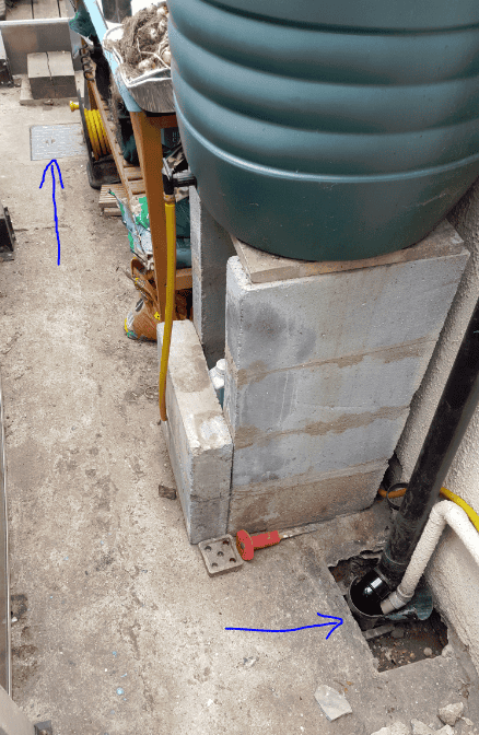 Side return of a Victorian terraced house showing a damp wall, an open gully at ground level with a black downpipe discharging into it, and blue arrows indicating the damp wall and the gully location.